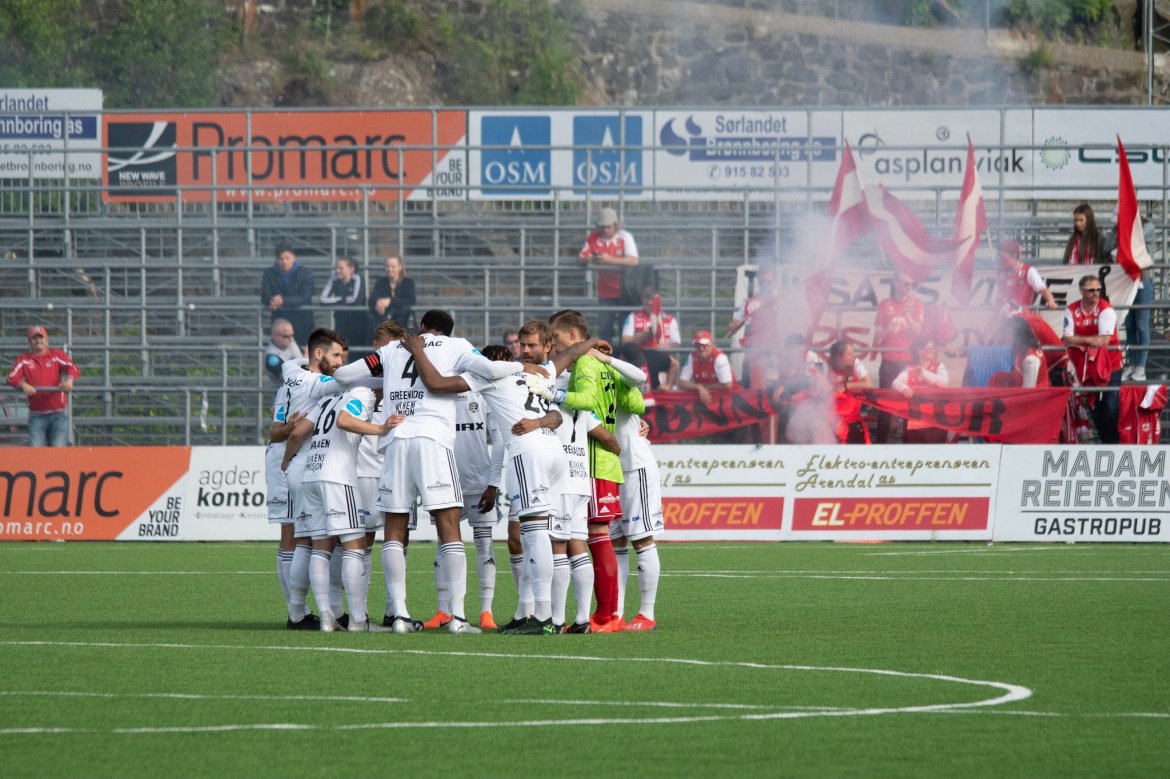 SAMMEN FOR ARENDAL: Hele laget i samlet konsentrasjon rett for avspark. I bakgrunnen bortesupportere fra B-gjengen på Bryne.